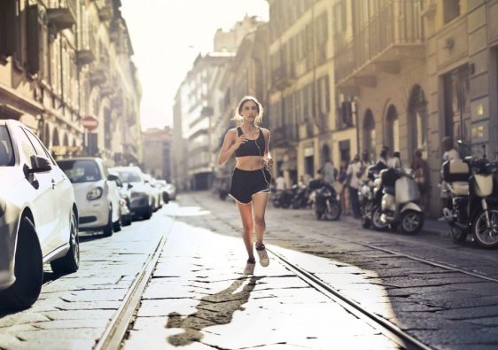 Energetic woman jogger running down a city street in active wear on a sunny day.